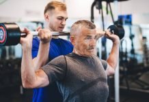 Image of a senior man lifting weights with help after he needed to find a personal trainer