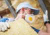 Image of a man installing loft insulation wearing a mask and hat using gloved hands to handled mineral rock wool insulation
