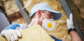 Image of a man installing loft insulation wearing a mask and hat using gloved hands to handled mineral rock wool insulation
