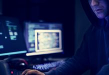 Dark picture of a hacker involved in identity theft and identity fraud wearing a hoodie and using a computer in a dark room