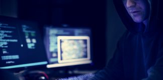 Dark picture of a hacker involved in identity theft and identity fraud wearing a hoodie and using a computer in a dark room