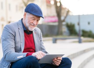Image of a senior man in city with phone and laptop sitting outside using public wifi