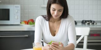 Image of a woman sitting in a kitchen using a smartphone to record drinking an orange juice into her diet apps