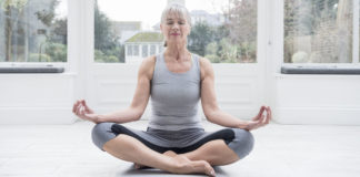 Senior woman sitting cross legged meditating ti improve concentration at home