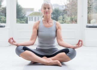 Senior woman sitting cross legged meditating ti improve concentration at home