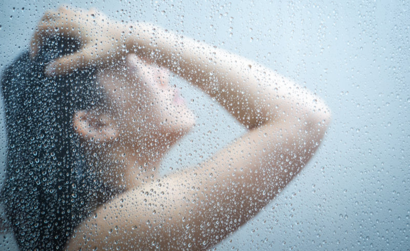 Women taking shower close up with a water drop on glass door.