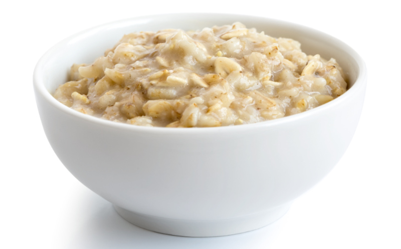 Prebiotic foods – Cooked whole porridge oats in white ceramic bowl isolated on white.