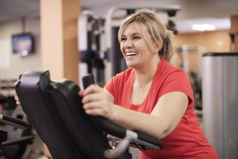 Happy woman riding on exercise bike at the gym