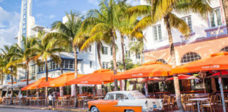 Miami Holidays 2020 Miami Beach, Florida, USA - April 25, 2016: View along Ocean Drive along South Beach Miami in the historic Art Deco District with hotels, restaurant, people and classic car visible. South Beach has been a notable tourist destinations for many years.