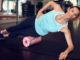 Foam roller back exercises Woman in mint sleeveless shirt and black leggings in gym doing exercise with foam or fascia roll and looking at camera.