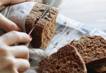 Health benefits of rye bread The girl cuts whole-wheat rye bread on a wooden table.