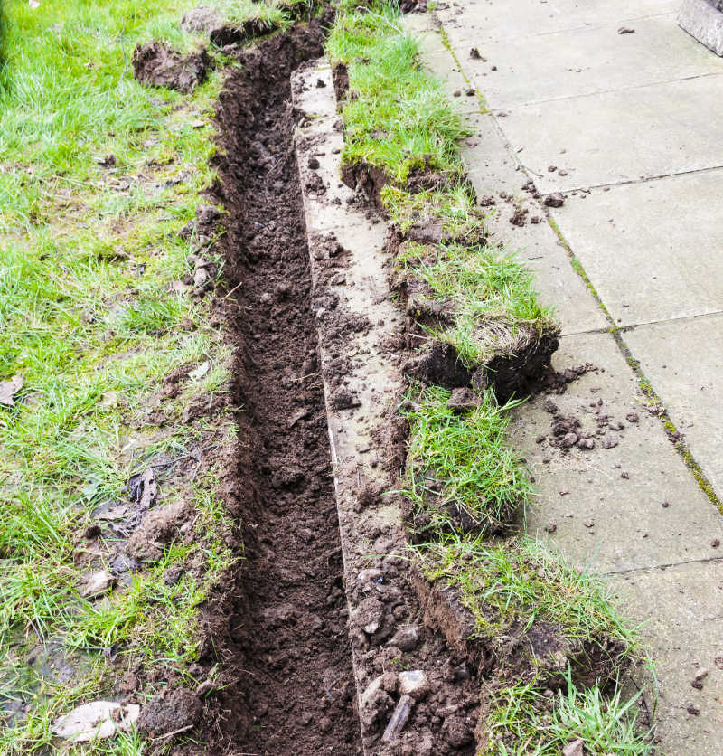 Trench dug at the bottom of a lawn to install a drainage channel.