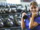 Gym confidence Middle aged Hispanic woman at a gym working out, lifting hand weights. She has a dumbbell in each hand, strengthening her arms and biceps. She is smiling at the camera.