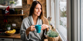 Slow living woman looking out of a window holding coffee cup