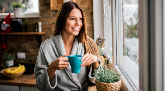 Slow living woman looking out of a window holding coffee cup