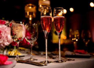 Two Flutes of Rose Champagne on a table with water glasses, candles, and flowers