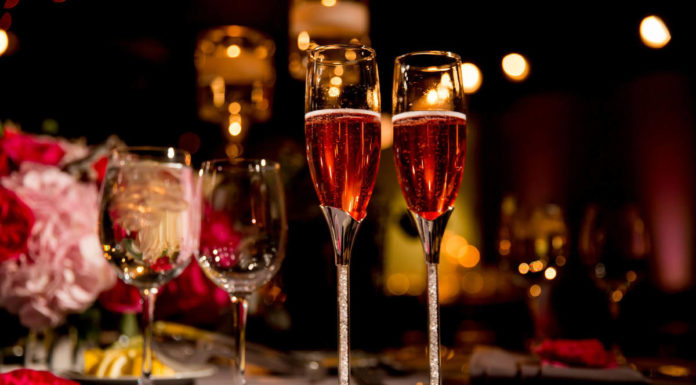 Two Flutes of Rose Champagne on a table with water glasses, candles, and flowers