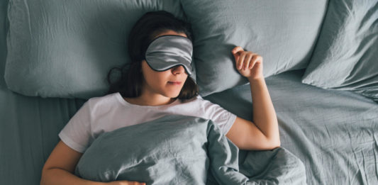 Woman sleeping in eye patch in grey bed.