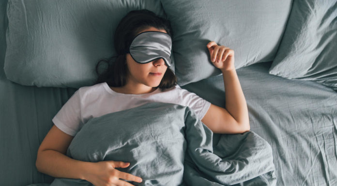 Woman sleeping in eye patch in grey bed.