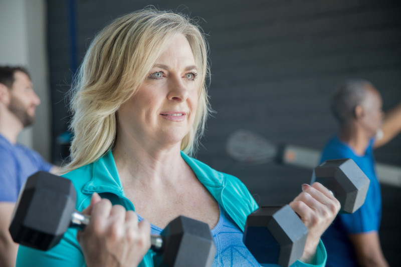 Mature woman smiling while lifting weights in busy gym