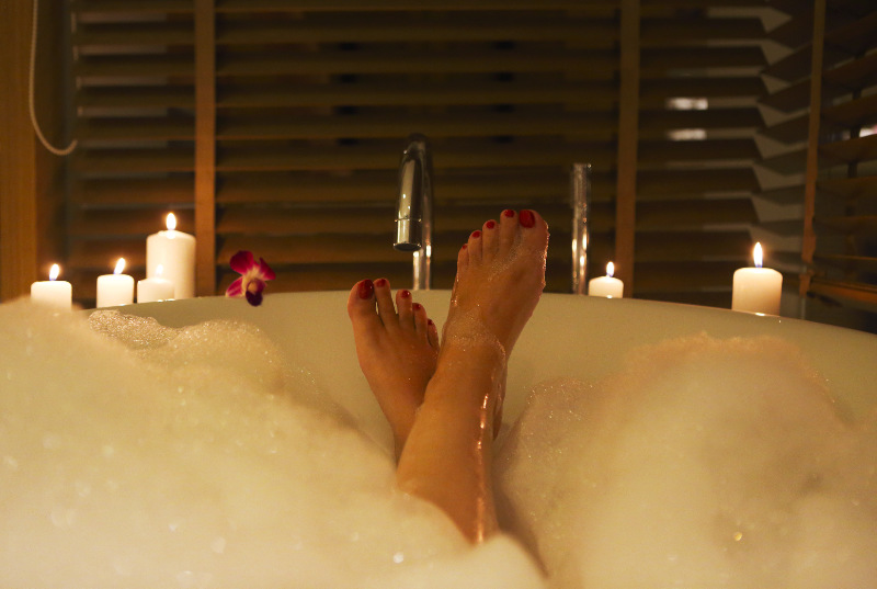 Back view of the feet of the young woman in bath with foam and candles