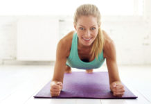 Portrait shot of attractive middle aged woman doing plank exercises on yoga mat in the fitness studio.