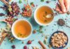 Health benefits of herbal tea Two cups of healthy herbal tea with mint, cinnamon, dried rose and camomile flowers in spoons and man's hand holding spoon of honey, blue background, top view