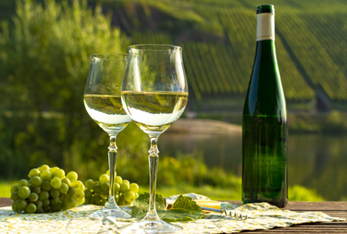 Famous German quality white wine riesling, produced in Mosel wine regio from white grapes growing on slopes of hills in Mosel river valley in Germany, bottle and glasses served outside in Mosel valley