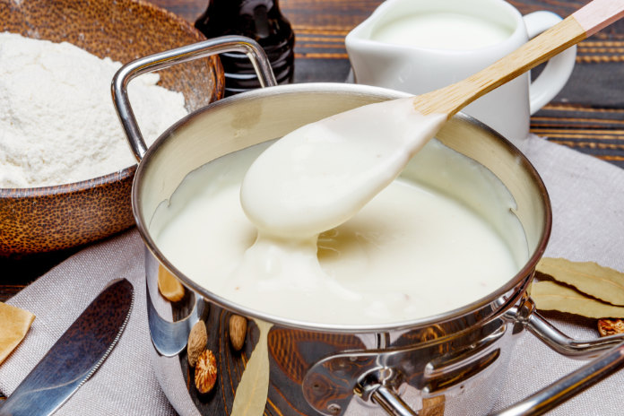 Preparation of bechamel sauce in a pan and ingredients on the wooden table