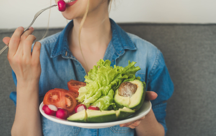 young woman eating fresh vegetables at home. Vegan eating avocado, salad, radish and tomatoes