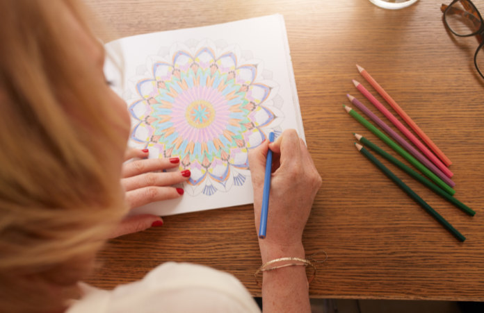 Overhead view of woman drawing in adult coloring book with color pencils. Anti stress exercise at home.