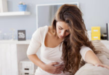 What is e.coli - Young woman sitting on the bed with hard stomach pain