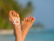 Woman foot with sun-shaped sun cream in the tropical beach
