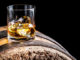 Glass of whiskey with ice on wooden barrel