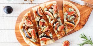 Ways to eat figs – Autumn flat bread pizza with figs, caramelized onions, blue cheese and rosemary. Top view table scene on a white wood background.