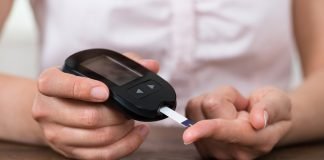Close-up Of Person Hands Holding Glucometer At Desk