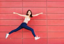 Excited girl is jumping against a red wall
