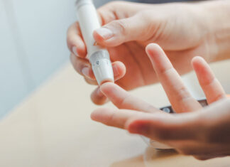 Diabetes close up of woman hands using lancet on finger to check blood sugar level by Glucose meter