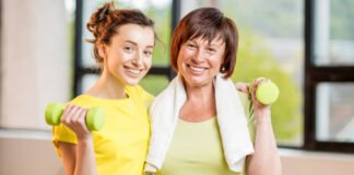 Exercise with a friend Young and older women in sportswear training with dumbbells indoors on the window background