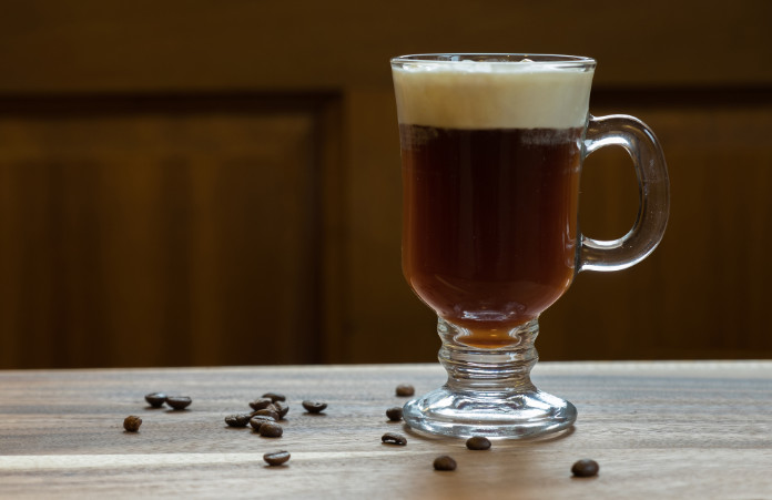 Making an Irish coffee – Glass of Irish coffee drink on wooden table with brown background