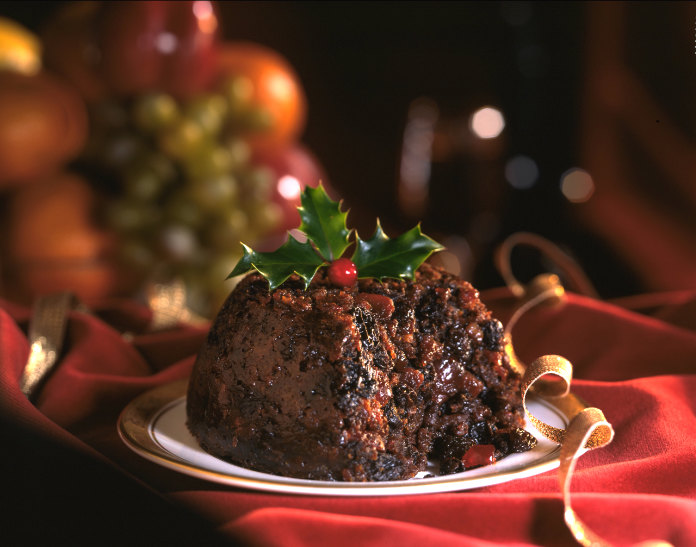 Traditional Christmas food Christmas Pudding decorated with holly leaves on red background