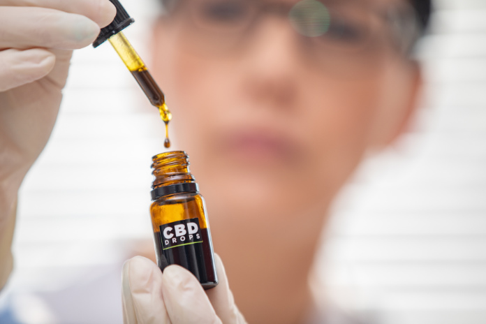 Close-up of Adult Woman Holding CBD Oil Drops and Looking at Them.
