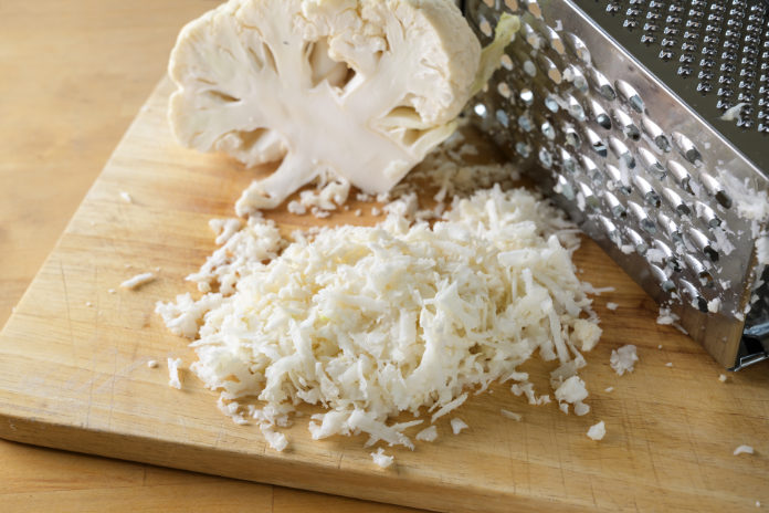 Grating cauliflower with a metal grater on a wooden kitchen board