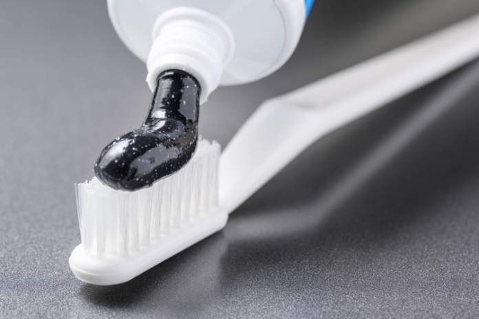 Close-up view of black charcoal toothpaste being squeezed on a white toothbrush.