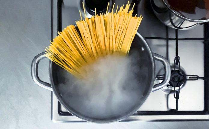 Cooking raw spaghetti in the boiling water contained in a saucepan. Italian cuisine. Raw food. interior of a domestic kitchen. Food preparation and cooking