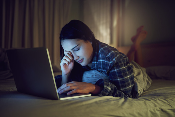 Shot of a sleepy young woman using a laptop late at night while lying on her bed in her bedroom