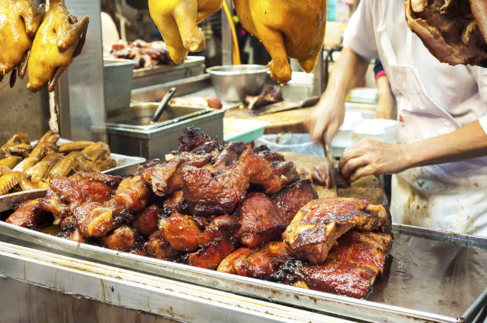 Butcher cutting barbequed pork, also known as cha siu, at a Hong Kong meat stall