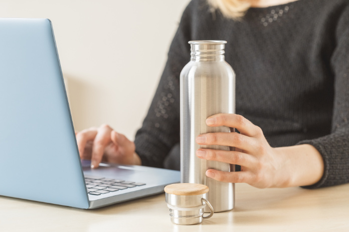 White woman holding her personal stainless steel water bottle on the working table.