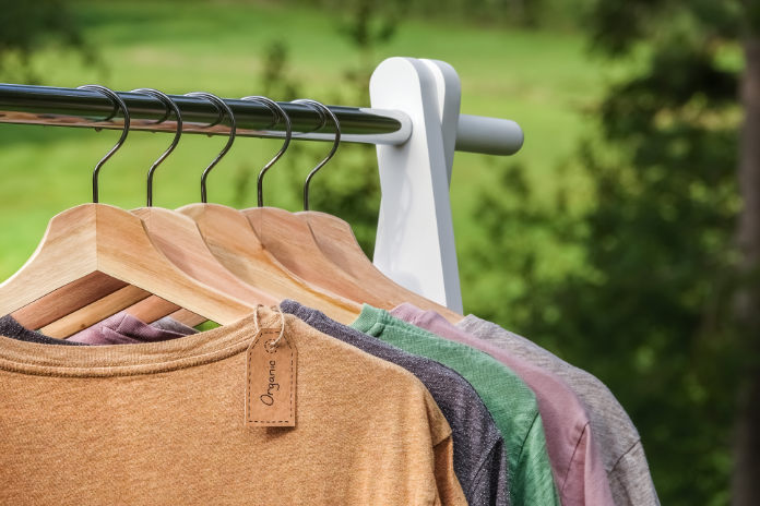 Organic clothes. Natural colored t-shirts hanging on wooden hangers in a row. 
