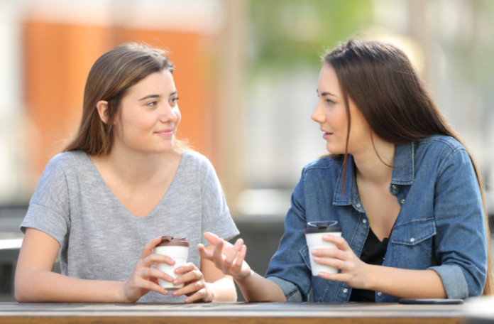 Two friends talking in a park drinking coffee